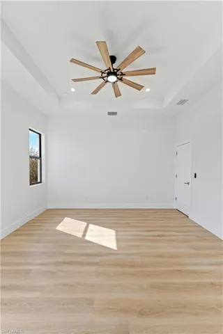 Spare room with a tray ceiling, light wood-type flooring, ceiling fan, and recessed lighting