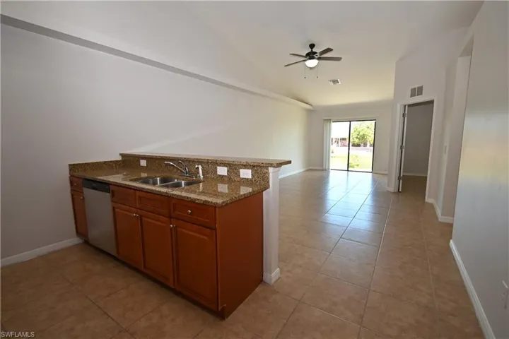 Kitchenette featuring a stainless steel double sink and dishwasher, wood cabinetry, and a granite-style countertop with a breakfast bar