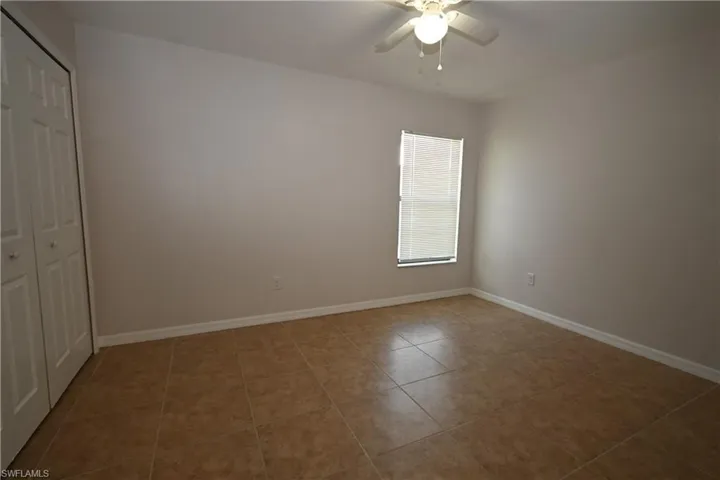 Neutral-toned room featuring a ceiling fan with light fixture, tile flooring, and a single window with blinds