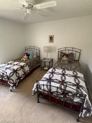 Bedroom with light colored carpet, a ceiling fan, and two single beds.