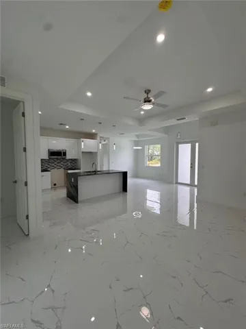 Kitchen with sink, an island with sink, a tray ceiling, decorative backsplash, and white cabinets