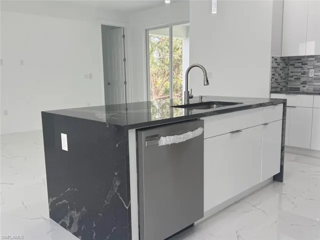 Kitchen featuring white cabinetry, sink, tasteful backsplash, stainless steel dishwasher, and an island with sink