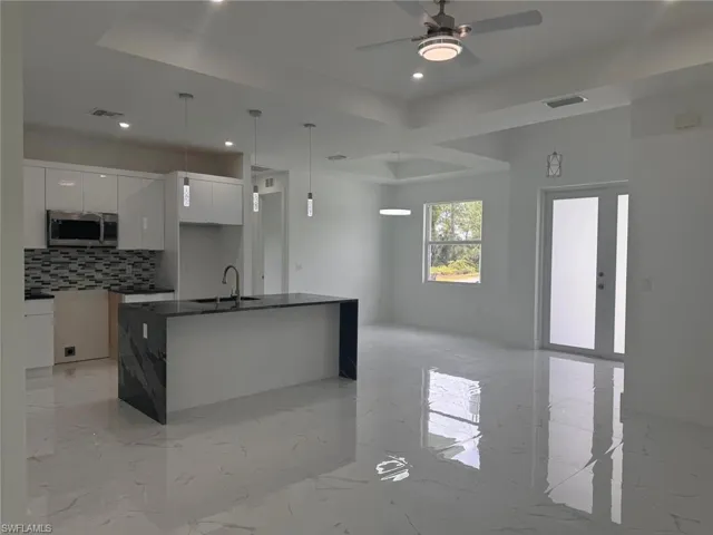 Kitchen with white cabinetry, ceiling fan, backsplash, an island with sink, and decorative light fixtures