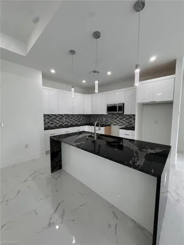 Kitchen with decorative backsplash, pendant lighting, white cabinetry, and dark stone counters