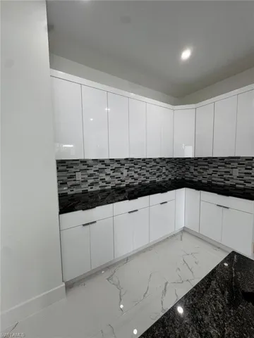 Kitchen featuring white cabinets, dark stone counters, and tasteful backsplash