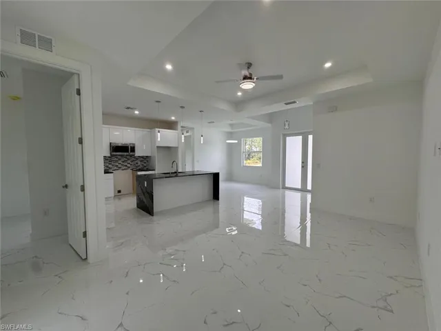 Kitchen with ceiling fan, backsplash, an island with sink, a tray ceiling, and white cabinets