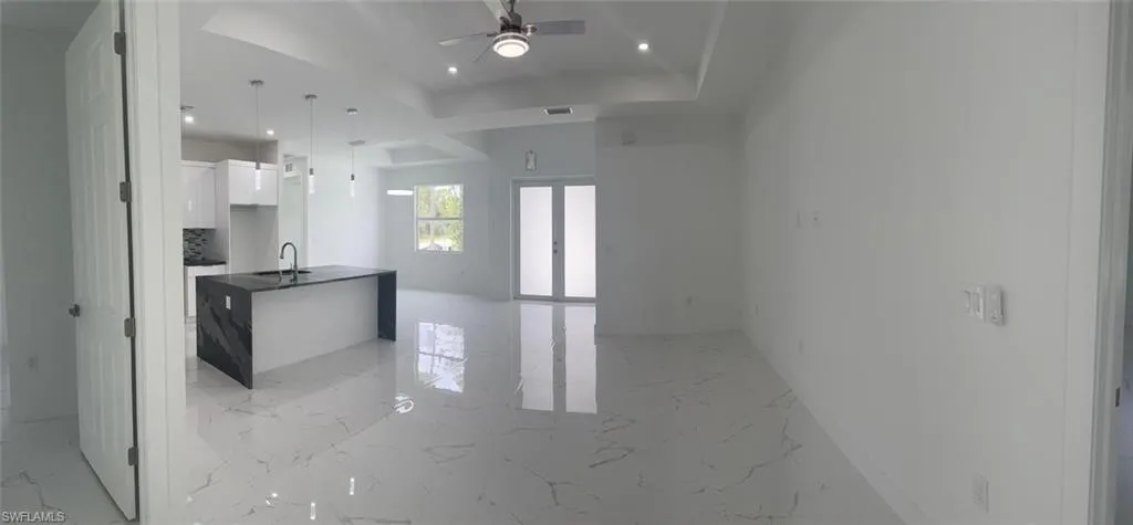 Kitchen with white cabinetry, sink, a center island, ceiling fan, and a tray ceiling