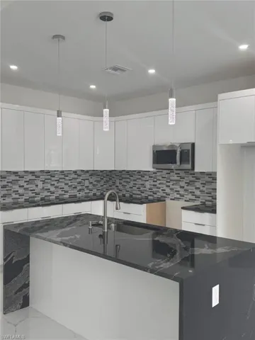 Kitchen featuring dark stone counters, decorative backsplash, white cabinets, and hanging light fixtures