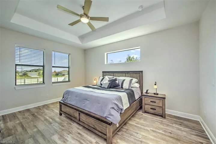 Bedroom with ceiling fan, a raised ceiling, multiple windows, and wood-type flooring