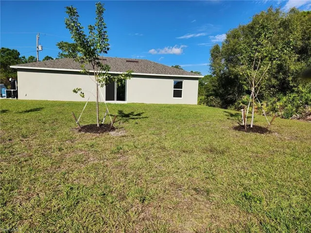 Rear view of property featuring a lawn, stucco siding, and a shingled roof