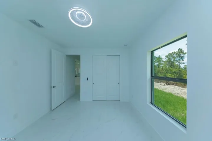 Light-filled interior space featuring a single window, white walls, and large format white tile flooring