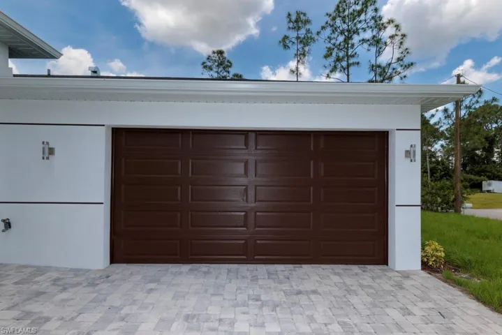 Garage entry featuring a paneled brown door and a light-toned paver driveway