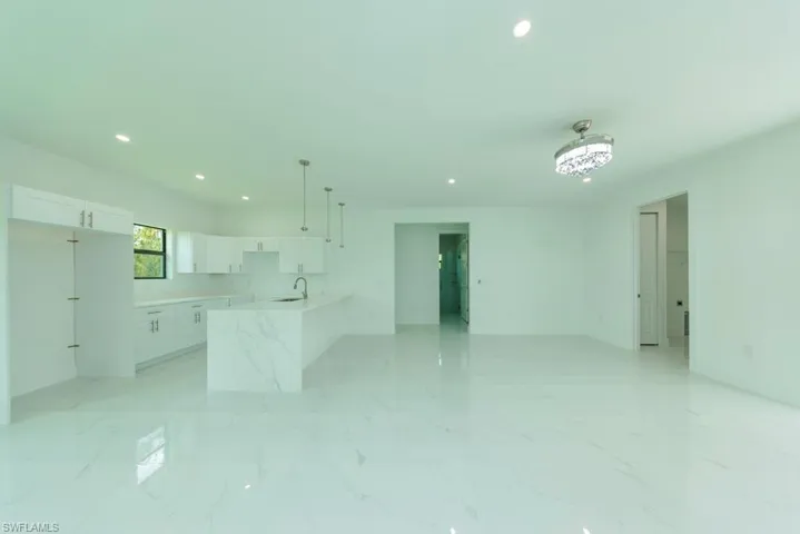 Open-concept living area featuring large format white tile flooring with subtle veining, recessed lighting, and a modern chandelier