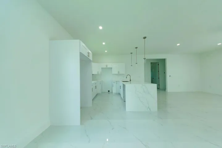 Open-concept kitchen featuring an oversized island with waterfall-edge countertop, white shaker-style cabinetry, a stainless steel sink with gooseneck faucet, and recessed lighting
