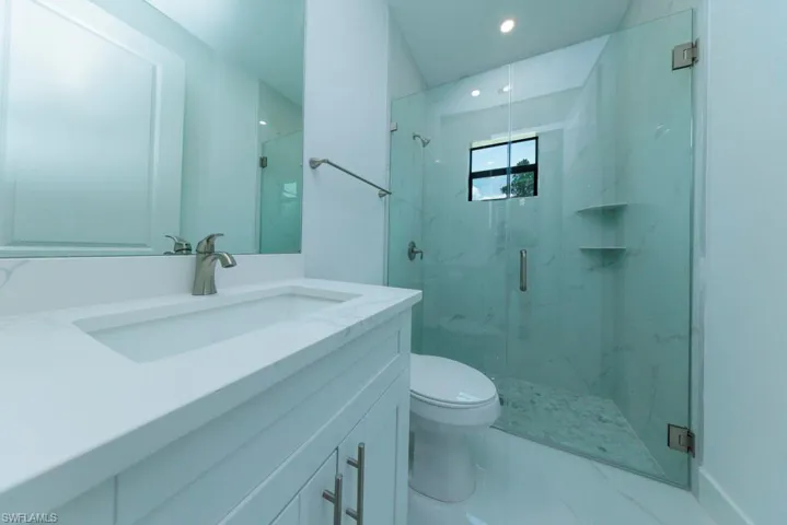 Contemporary bathroom featuring a frameless glass shower enclosure, a single vanity with an integrated sink, a large wall mirror, and recessed lighting