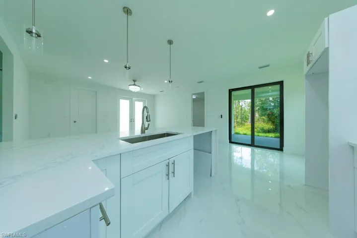 Kitchen island featuring a stainless steel sink, a gooseneck faucet, and quartz countertops with white cabinetry