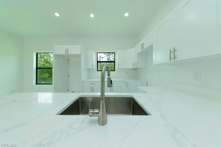 Kitchen featuring a large undermount stainless steel sink with a brushed nickel pull-down faucet, white shaker-style cabinetry, and white countertops with subtle veining