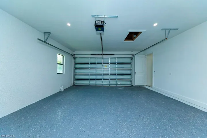Spacious garage featuring an epoxy-coated floor, automatic garage door opener, recessed lighting, and a side entry door