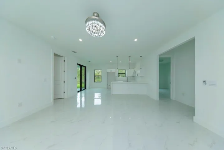 Spacious open-concept living area featuring large format white tile flooring, recessed lighting, and a modern chandelier