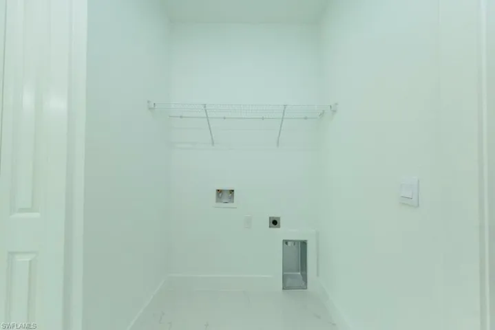 Utility space featuring white walls, white trim, white flooring, and a wire storage shelf