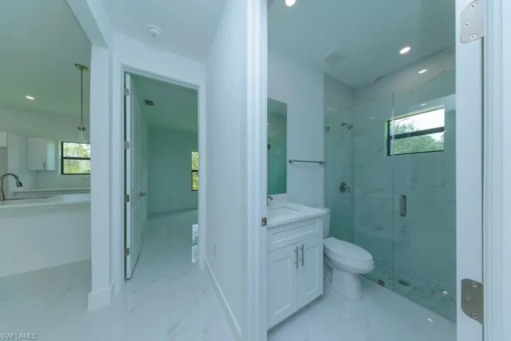 Contemporary bathroom featuring a glass-enclosed shower with tiled walls, a single vanity with a white cabinet, and recessed lighting