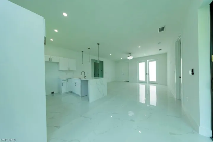 Open-concept interior featuring white-finish cabinetry, a waterfall island, pendant lighting, recessed lighting, and French doors