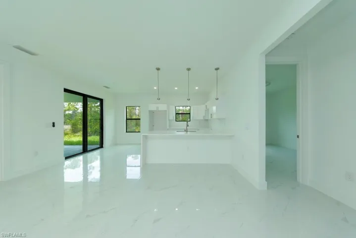 Open-concept living area featuring large format white tile flooring, a kitchen island with pendant lighting, white cabinetry, and a sliding glass door leading to the exterior