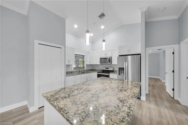 Kitchen featuring ornamental molding, white cabinetry, light stone countertops, hanging light fixtures, and stainless steel appliances