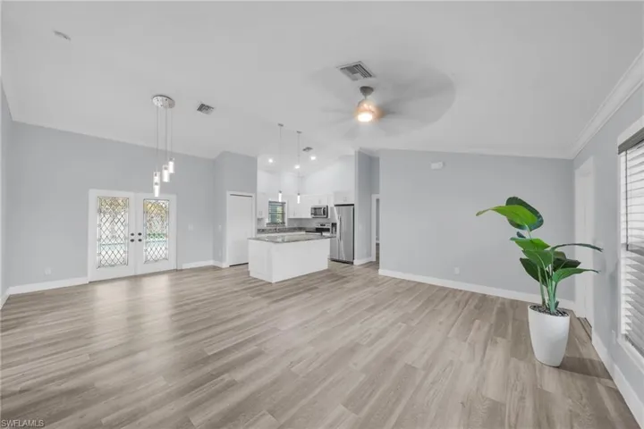 Unfurnished living room featuring vaulted ceiling, french doors, ornamental molding, light wood-type flooring, and a ceiling fan