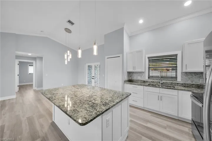 Kitchen featuring light stone countertops, a center island, vaulted ceiling, white cabinets, and light wood-type flooring