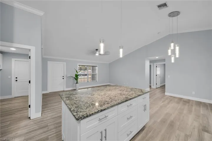 Kitchen featuring ornamental molding, light stone counters, hanging light fixtures, vaulted ceiling, and white cabinetry