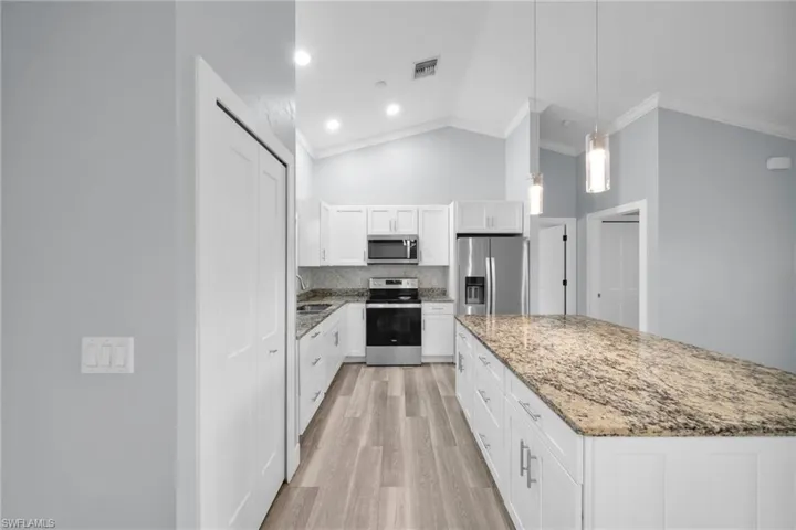 Kitchen with decorative light fixtures, stainless steel appliances, white cabinetry, a center island, and light stone countertops