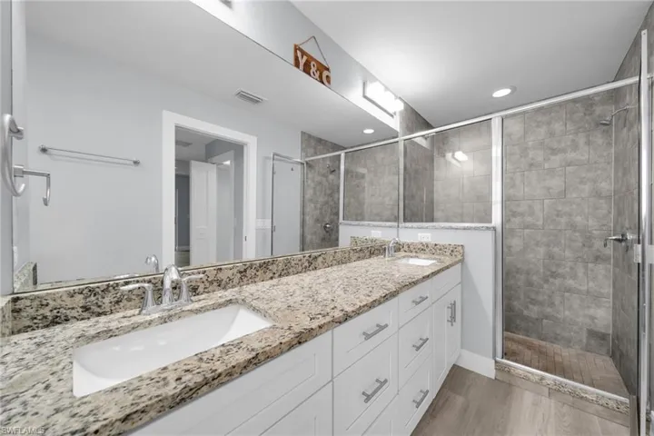 Bathroom with double vanity, a stall shower, light wood finished floors, and recessed lighting