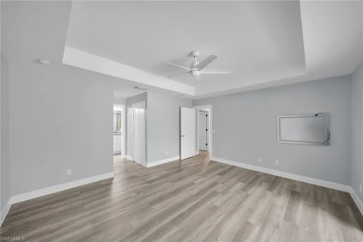 Unfurnished bedroom with a raised ceiling, a ceiling fan, light wood finished floors, and connected bathroom