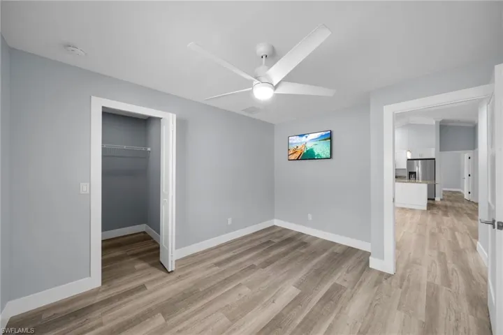 Unfurnished bedroom with a walk in closet, stainless steel refrigerator with ice dispenser, light wood finished floors, and a ceiling fan