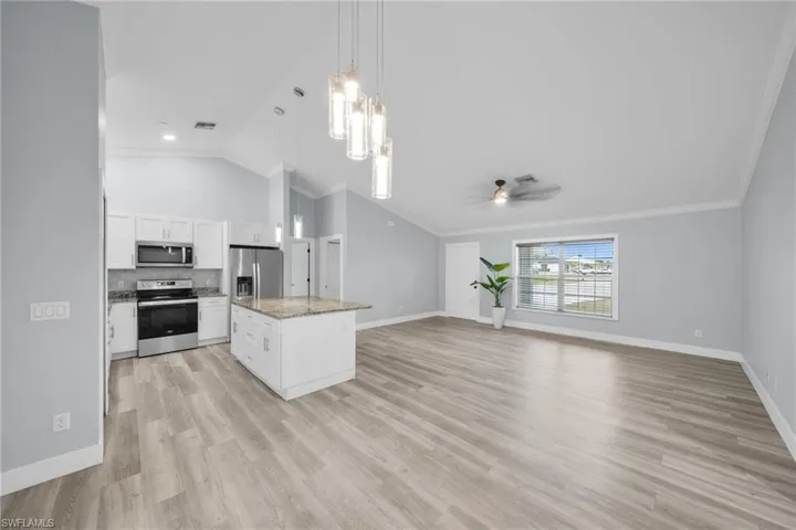 Kitchen featuring lofted ceiling, white cabinetry, appliances with stainless steel finishes, hanging light fixtures, and a chandelier