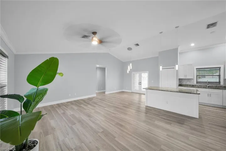 Unfurnished living room with ornamental molding, light wood-type flooring, vaulted ceiling, and a ceiling fan