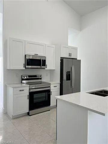 Kitchen featuring stainless steel appliances, a towering ceiling, white cabinetry, and light stone counters