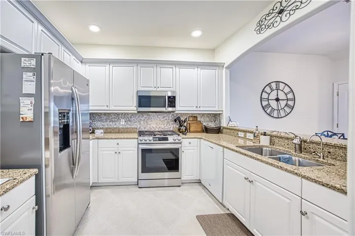 Kitchen featuring stainless steel appliances, white cabinetry, granite countertops, a mosaic tile backsplash, and light tile flooring