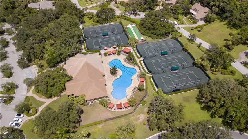 Expansive recreational area featuring a large clubhouse with a multi-gabled roof, a free-form swimming pool with surrounding lounge areas, multiple tennis courts, and a manicured green lawn area