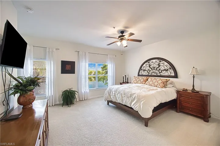 Spacious room featuring light-colored carpet, multiple windows with blinds, a ceiling fan with integrated lighting, and a wall-mounted television