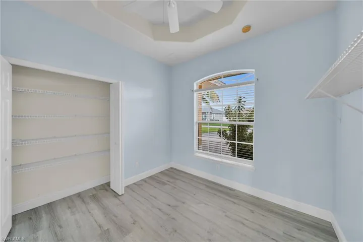 Unfurnished bedroom with a raised ceiling, a closet, light wood-style floors, and a ceiling fan