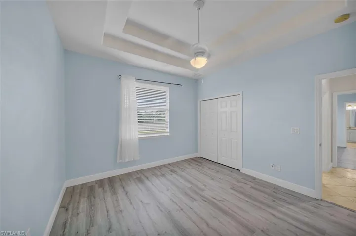 Unfurnished bedroom featuring a tray ceiling, light wood-type flooring, and a closet