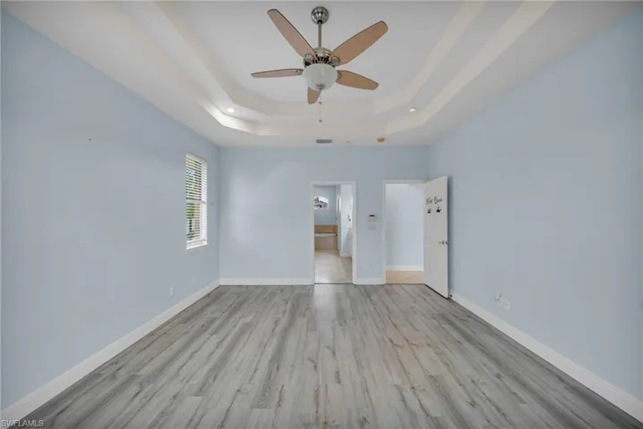 Unfurnished bedroom with light wood finished floors, a ceiling fan, ensuite bath, and a tray ceiling