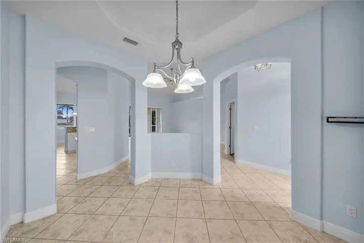 Unfurnished room featuring light tile patterned floors, a chandelier, arched walkways, and a tray ceiling