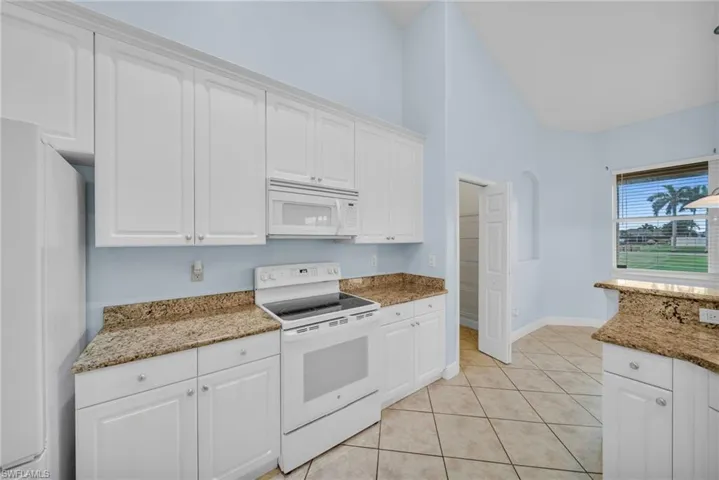 Kitchen featuring white appliances, light stone counters, white cabinetry, and a towering ceiling