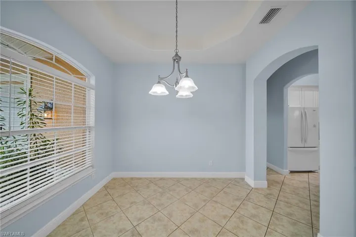 Unfurnished room with arched walkways, light tile patterned floors, a raised ceiling, and a chandelier