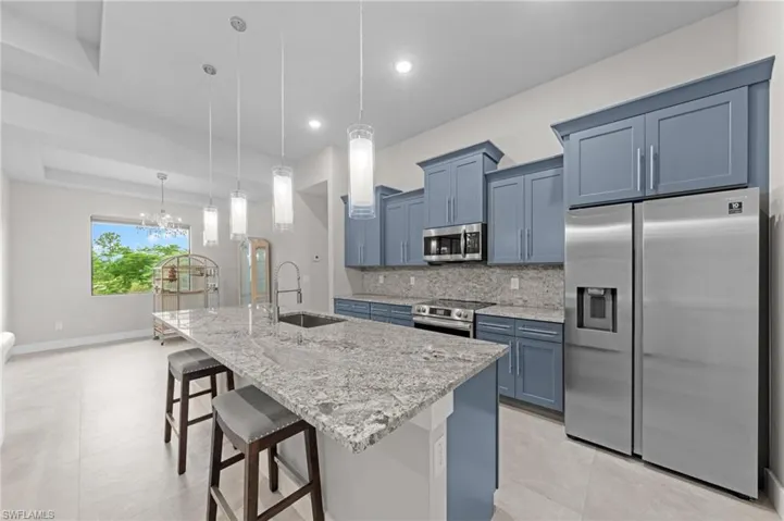 Kitchen featuring stainless steel appliances, backsplash, light stone counters, and light tile patterned floors