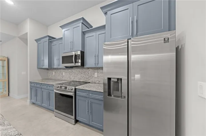 Kitchen featuring appliances with stainless steel finishes, backsplash, light stone counters, and blue cabinets