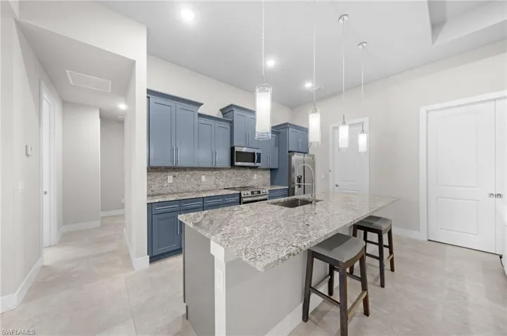 Kitchen with stainless steel appliances, a kitchen breakfast bar, backsplash, an island with sink, and pendant lighting